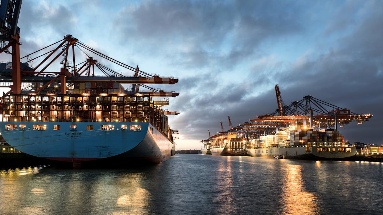 A scenic view of container ships docked at Hamburg Port during twilight, highlighting the bustling cargo terminal.