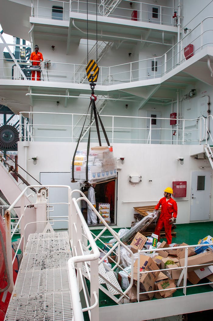 Cargo and maritime workers handling supply transfer on a ship deck.