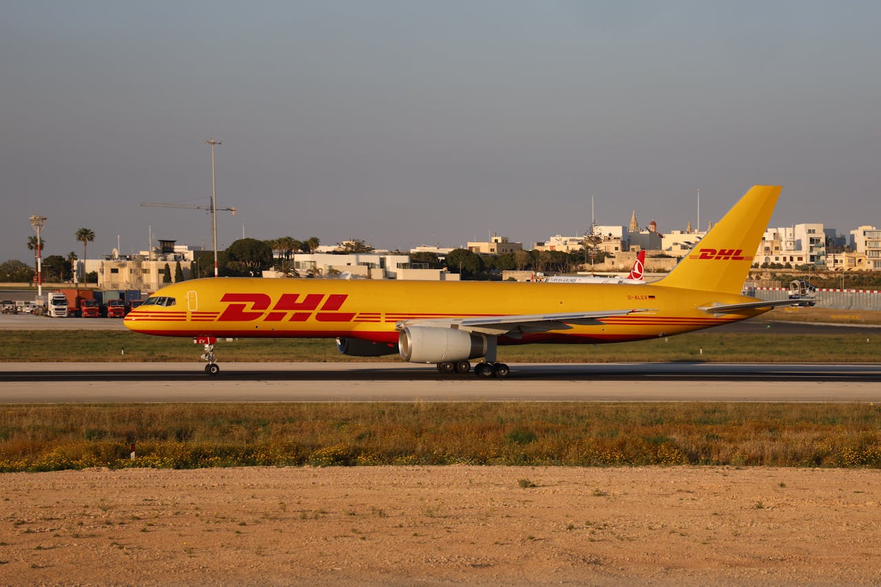 Yellow DHL cargo aircraft taxiing on airport runway in daytime.