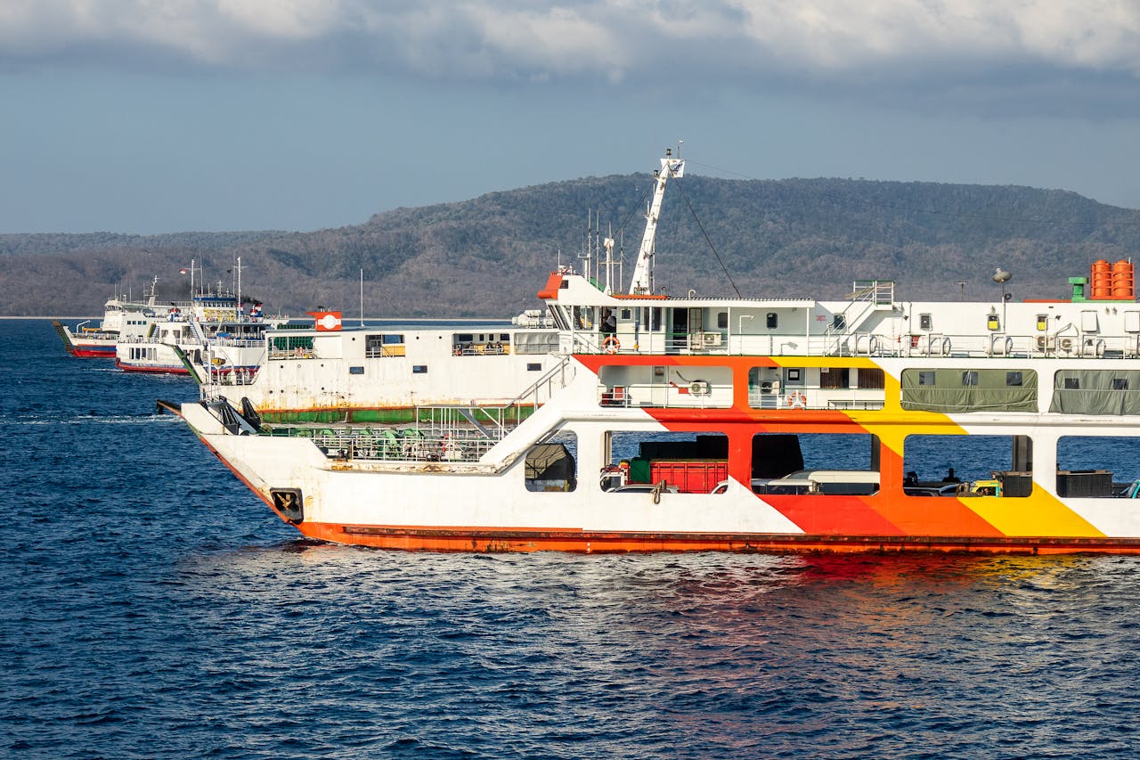 Vibrant ferries docked at a scenic harbor with mountains in the background, capturing coastal Indonesia's essence.